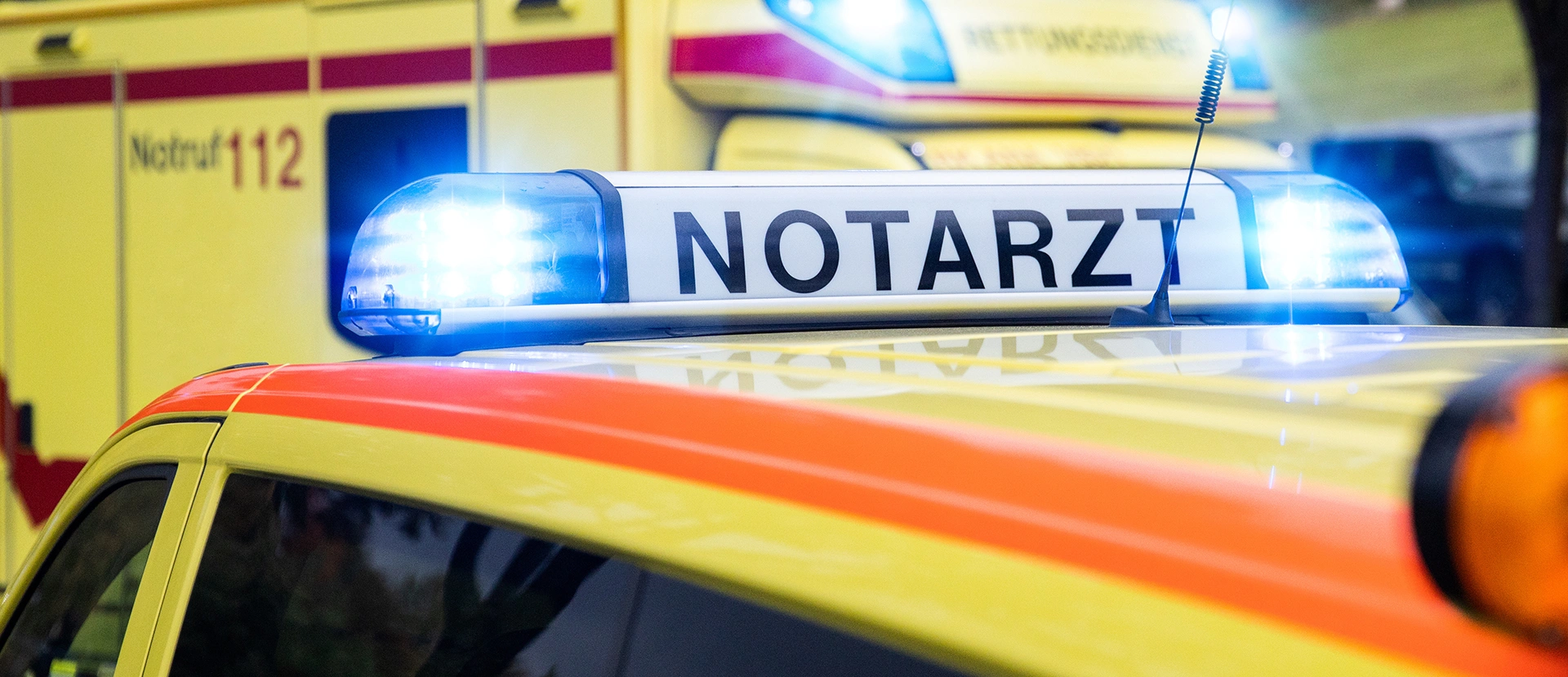 Martinshorn auf dem Dach eines Notarzteinsatzfahrzeuges mit Beschriftung "Notarzt" und dahinter stehend ein Rettungswagen.