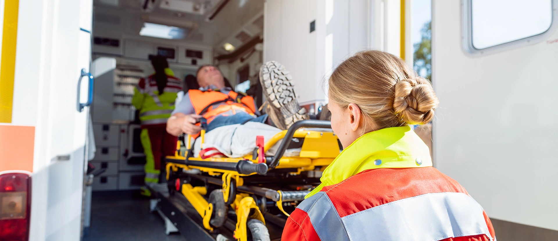 Rettungssanitäterin hebt Patienten auf Krankentrage in den Rettungswagen.